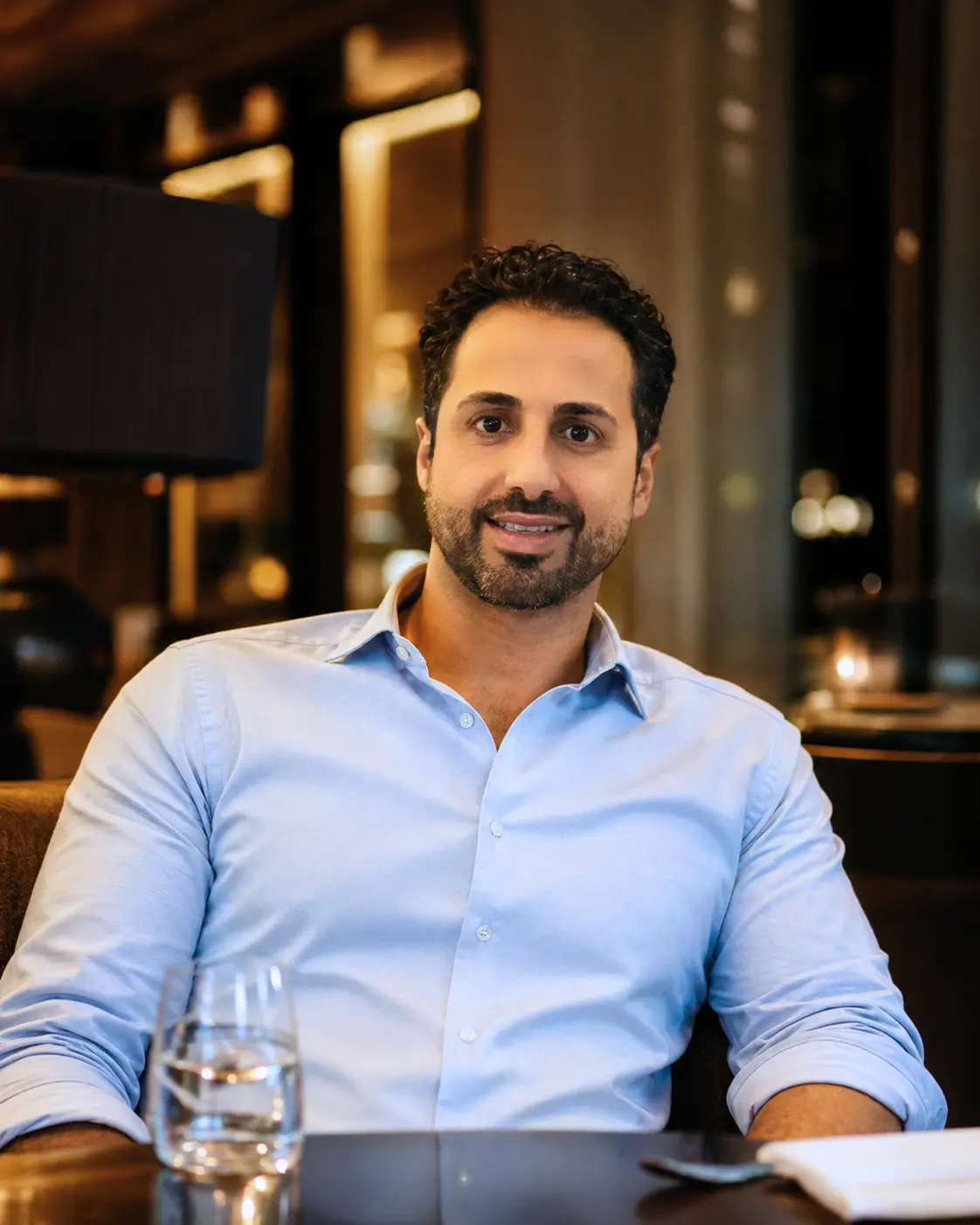 Andreas Tsiartas, founder of Rising with Atlas, seated at a table in a warm interior.